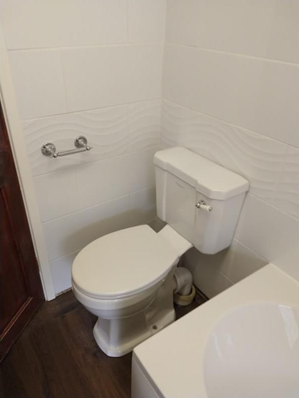 A close-coupled toilet against white wave-patterned tiling, with a chrome toilet roll holder beside it.