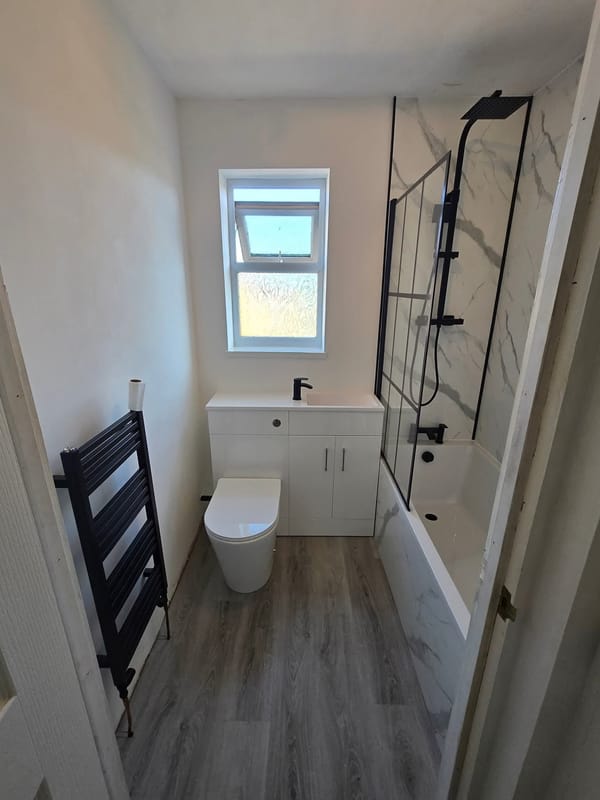 The same marble-effect bathroom from the doorway, showing the black ladder towel radiator on the near wall and the wood-effect floor.
