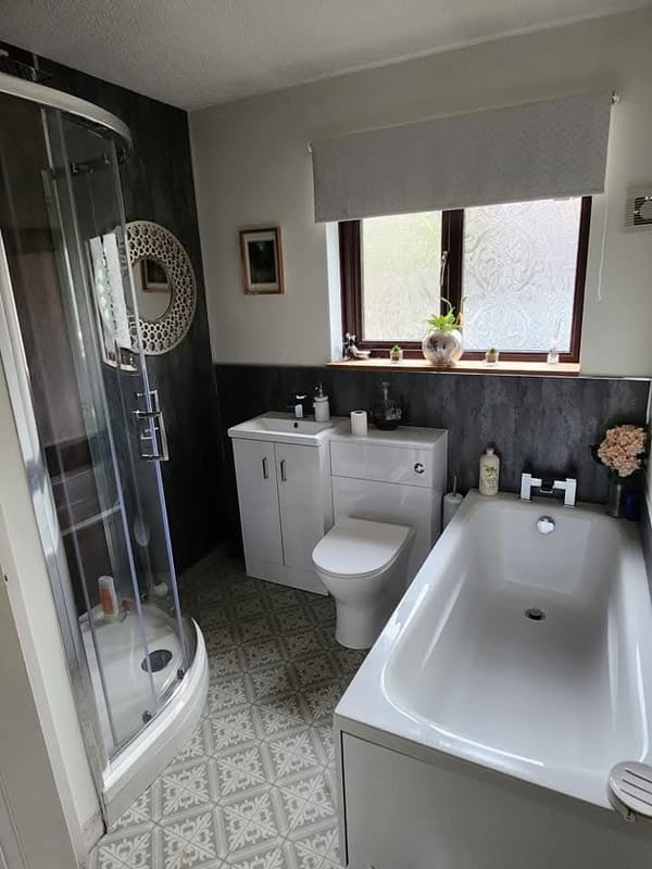 The room the enclosure is in: the quadrant shower on the left, a bath on the right, a vanity unit and toilet between them, and patterned floor tiles.