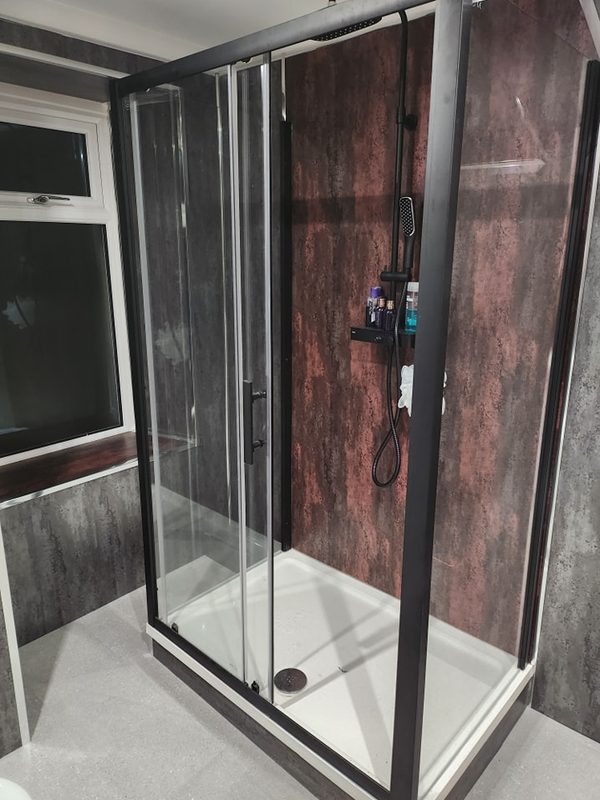 In its place, a large three-sided black-framed shower enclosure against grey concrete-effect and copper-effect wall panels.