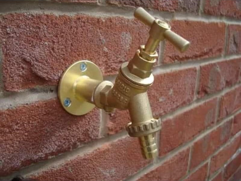 A brass outside tap on a brass wall plate, fitted to a red brick wall, with a hose connector screwed into the outlet.
