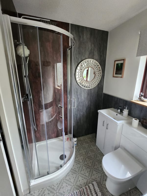 A quadrant shower enclosure with curved sliding doors, fitted against dark slate-effect wall panels.