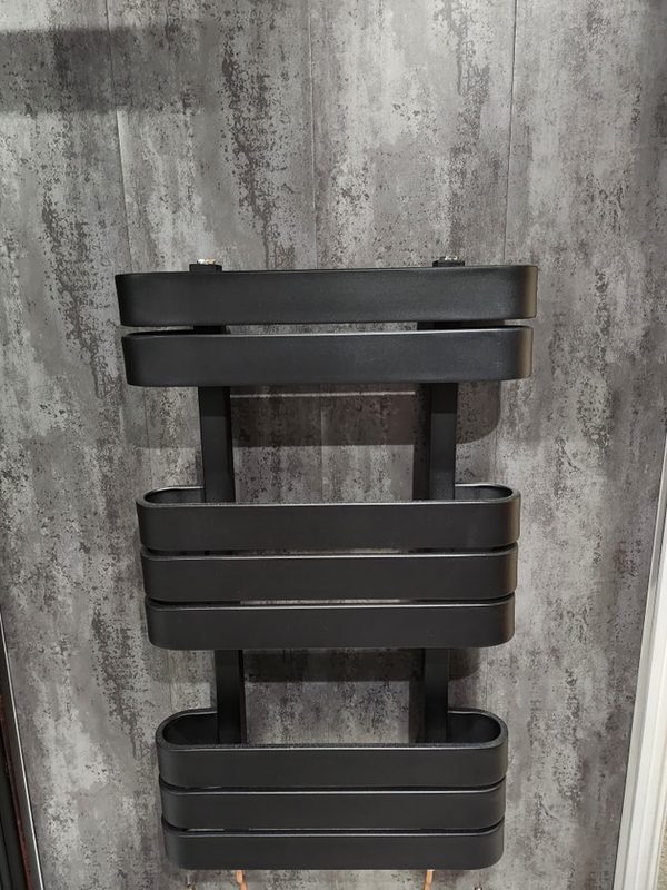 A matt black towel radiator with wide flat bars, mounted on grey concrete-effect wall panels.