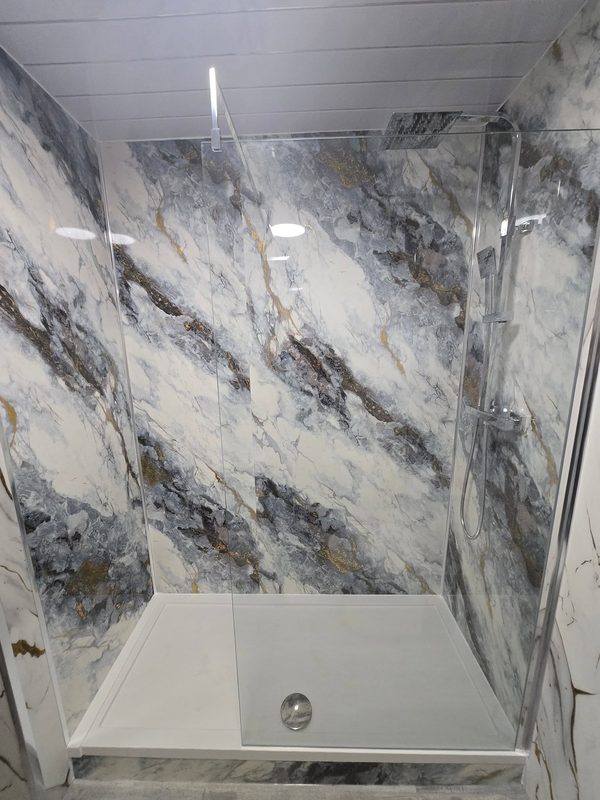 A walk-in shower with a low white tray and a glass screen, the walls in grey and gold marble-effect panels.