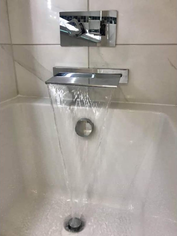 A chrome waterfall bath filler running into a white bath.